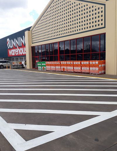 A large white pedestrian crossing on the road outside a Bunnings store.