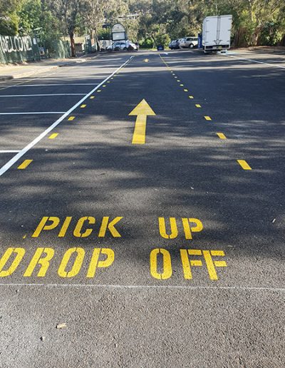 Directional arrows and words on road directing parents to school pick up/drop off area next to carparking area.
