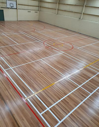 A mix of tennis, netball and basketball courts marked on the floor of an indoor stadium.